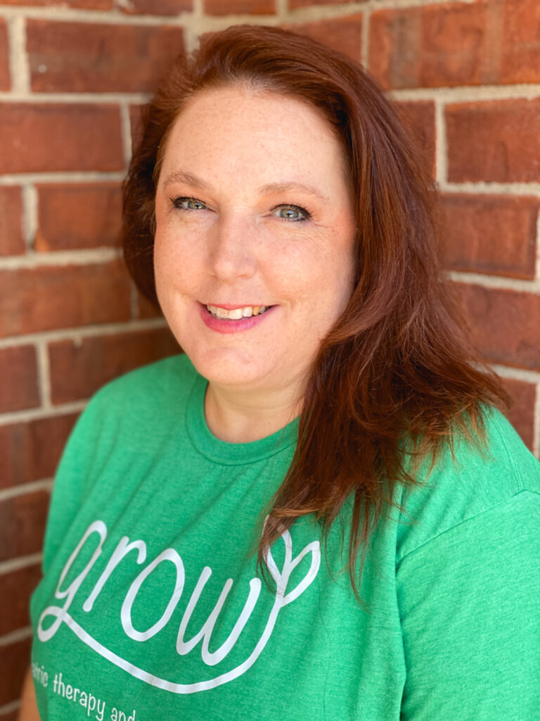 A portrait of Jenny Newton, COTA/L with shoulder-length red hair, wearing her green Grow t-shirt